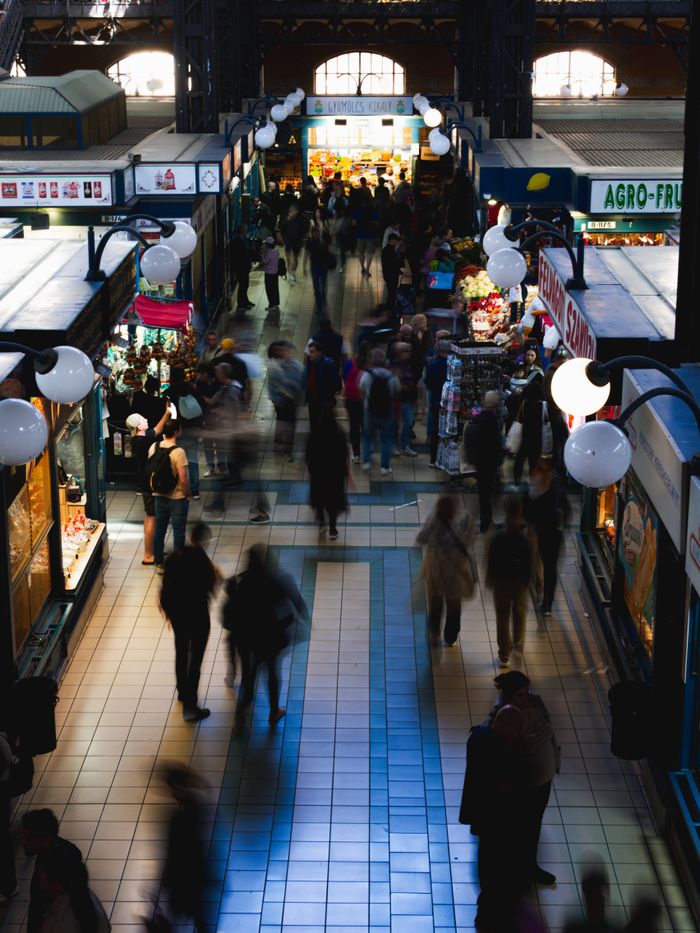 Home Blurred crowd in Budapest market hall, showcasing vibrant life.